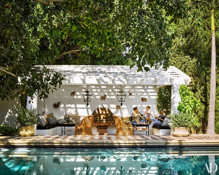 two people sitting on chairs in front of a swimming pool with trees and bushes surrounding them