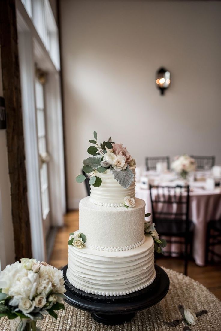 a wedding cake sitting on top of a table next to white flowers and greenery