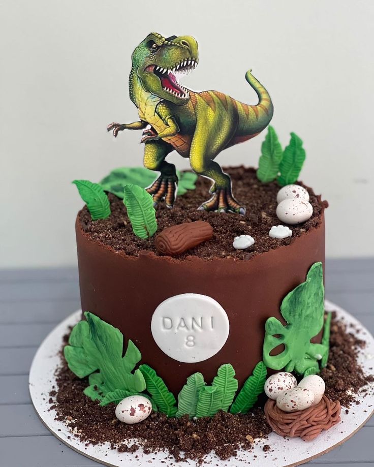 there is a cake with a dinosaur on top and eggs in the dirt next to it