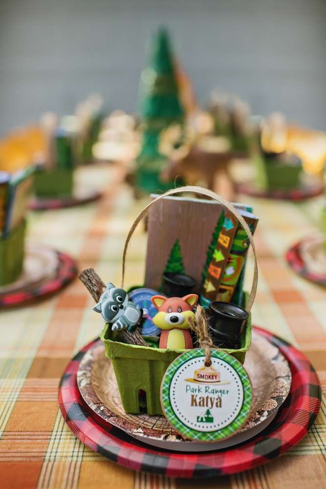 a table topped with plates and cups filled with food next to a forest themed centerpiece