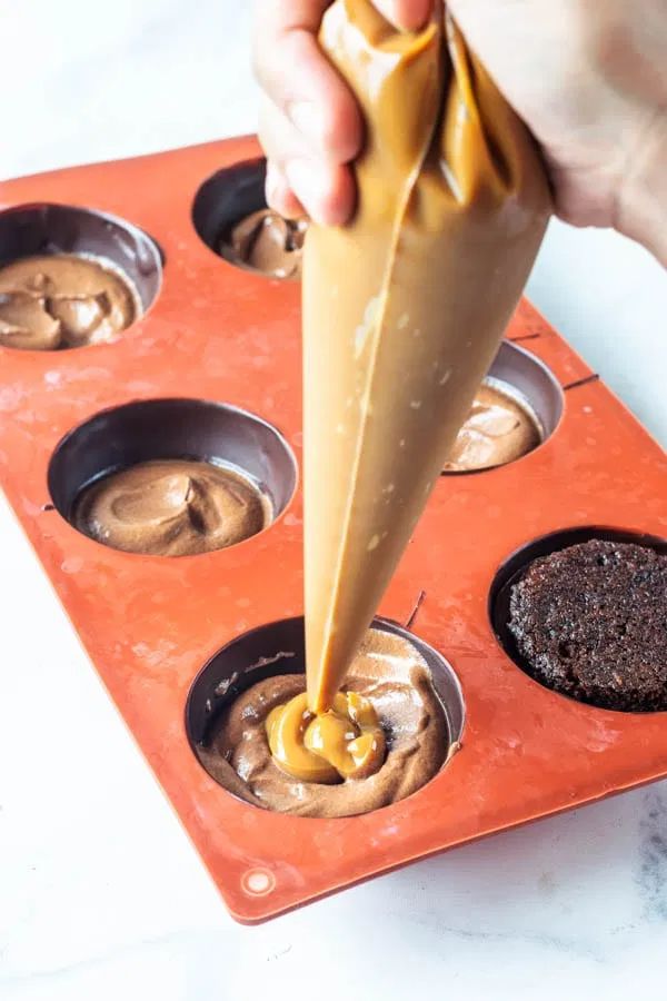 a person dipping something into a cupcake in a muffin tin with chocolate and caramel