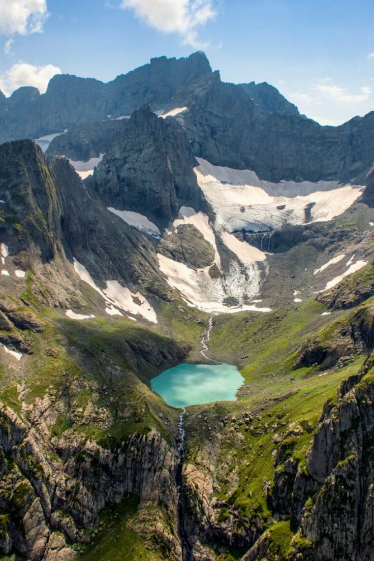 the mountains are covered in snow and green grass, with a lake surrounded by rocks