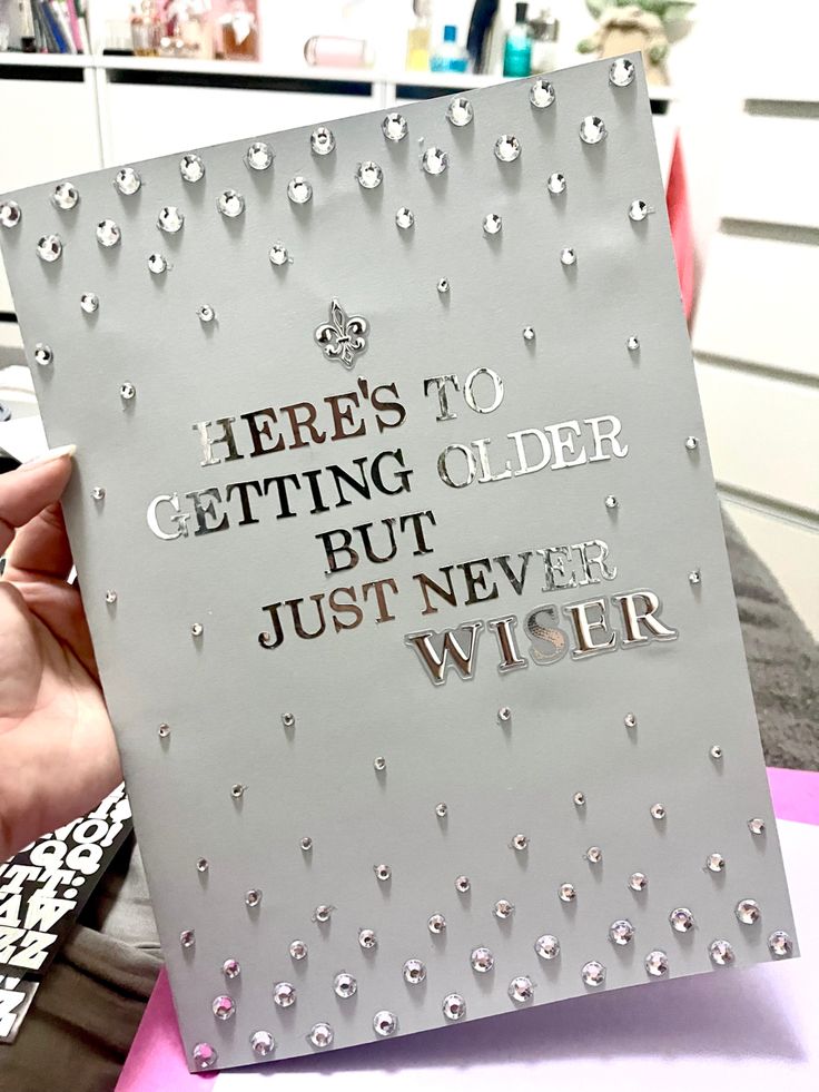 a person holding up a card that says here's to getting older but just never wider