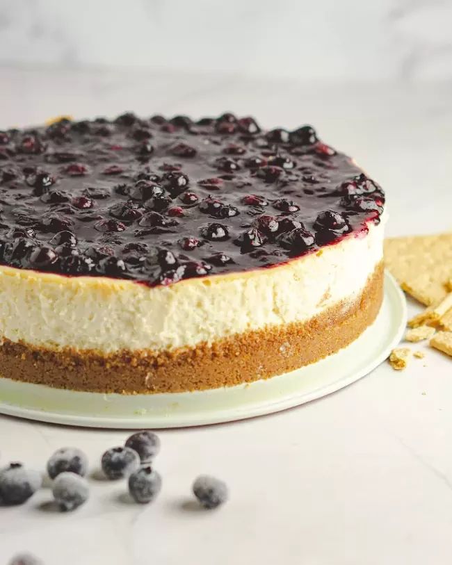 a cheesecake topped with blueberries on a plate next to crackers