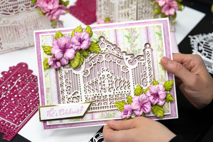 a person holding up a card with flowers on it and some doily around it