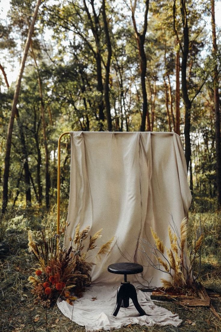 a chair sitting on top of a white sheet in the middle of a wooded area