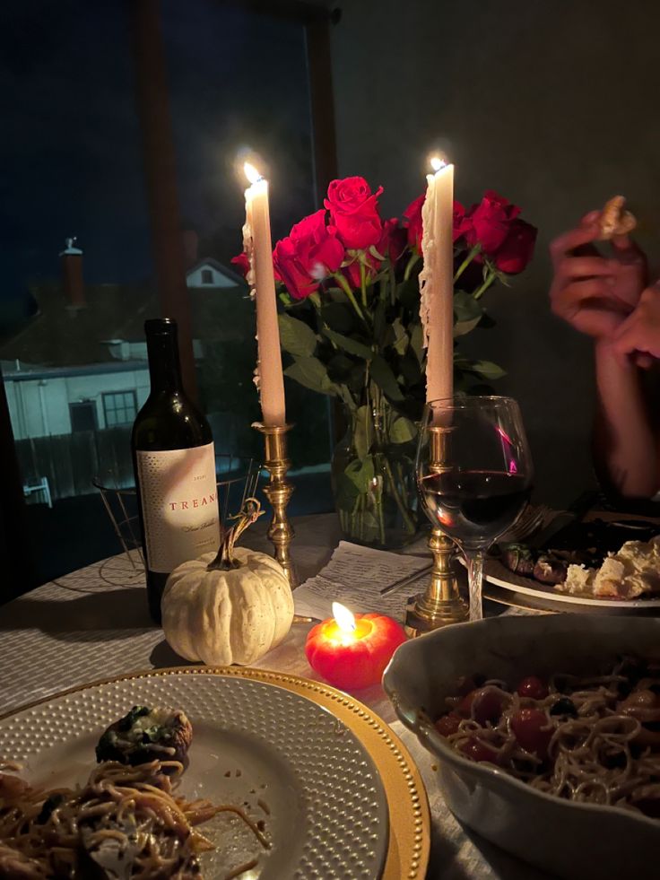 the table is set with food, wine and two candles in front of roses on it