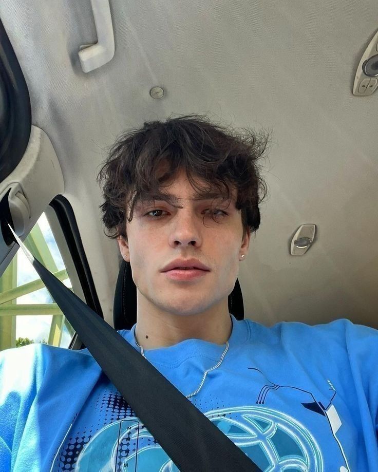 a young man sitting in the back seat of a car holding two large black scissors