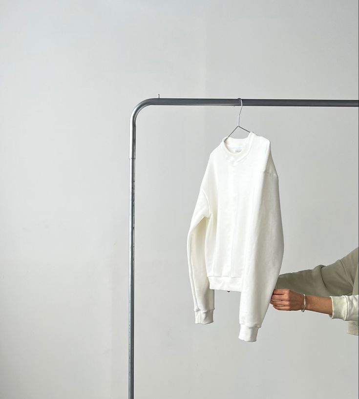 a white shirt hanging on a clothes rack in front of a person's hand