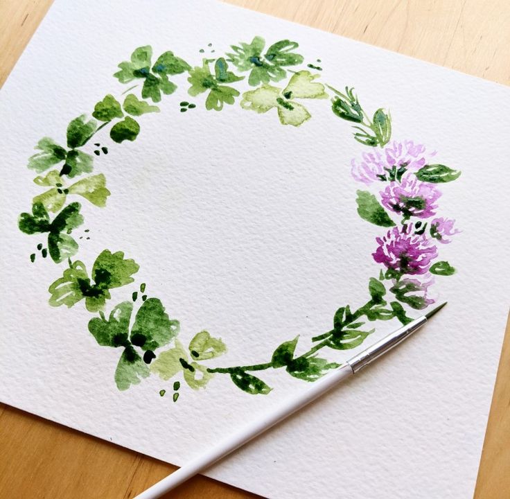 a watercolor painting of purple flowers and green leaves in a circle on white paper