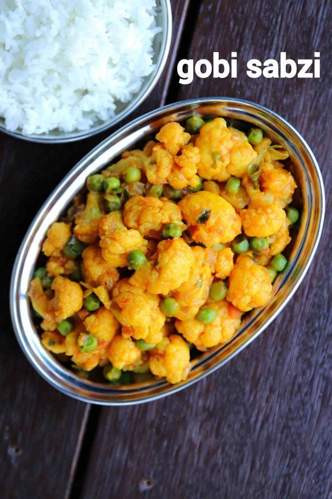 a bowl filled with cauliflower and peas next to rice on a wooden table