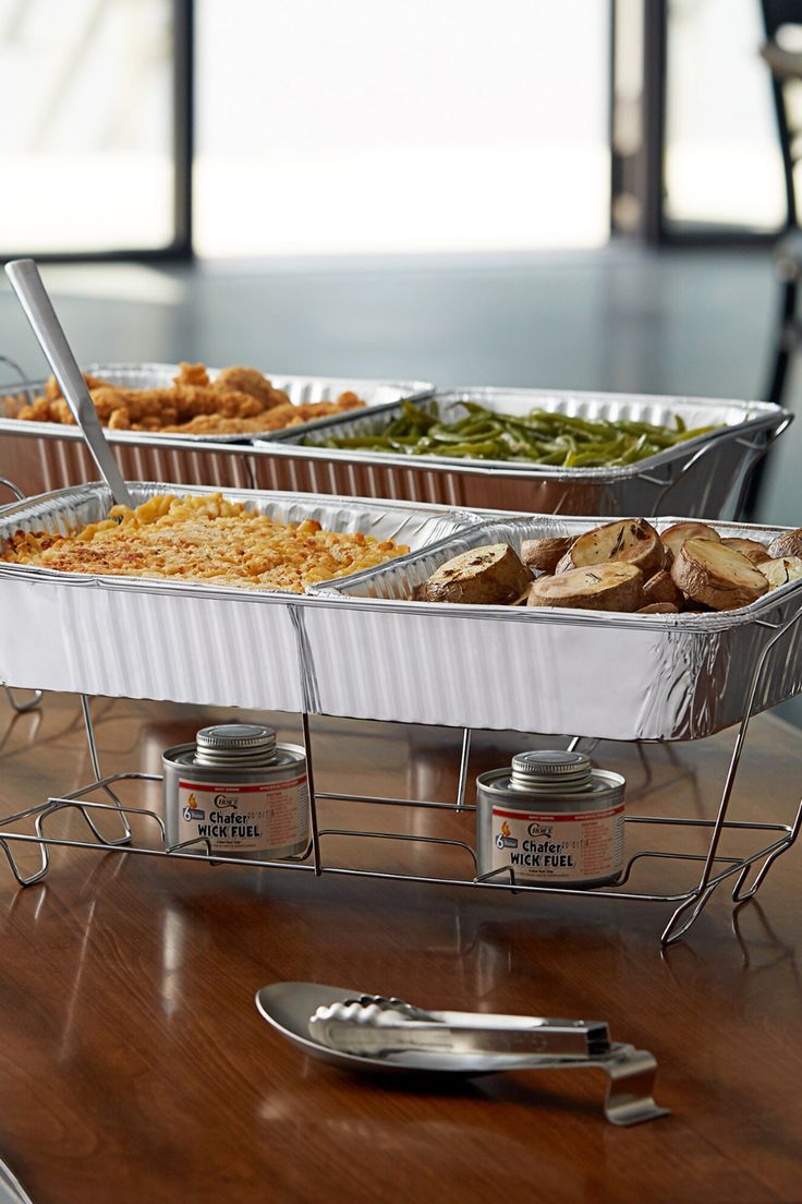 three trays of food sitting on top of a wooden table next to silver utensils