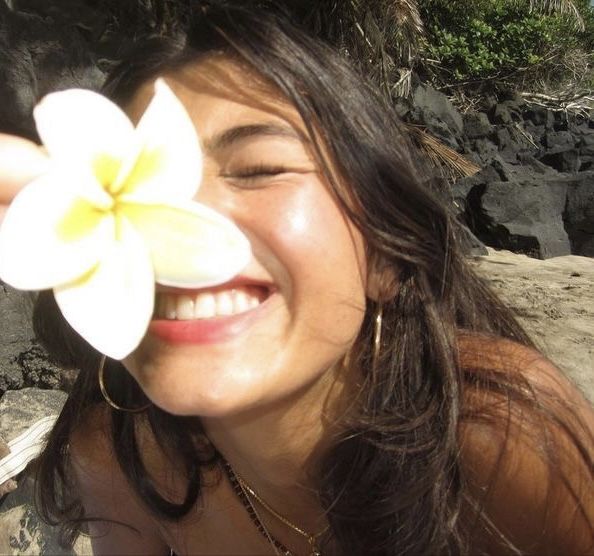 a woman is smiling and holding a flower in front of her face while laying on the beach