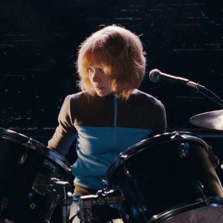 a woman is playing drums in front of a microphone