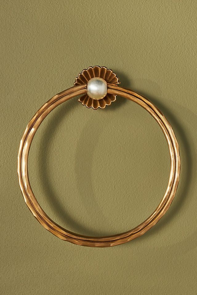 a gold ring with a pearl hanging from the middle, on a green wall background