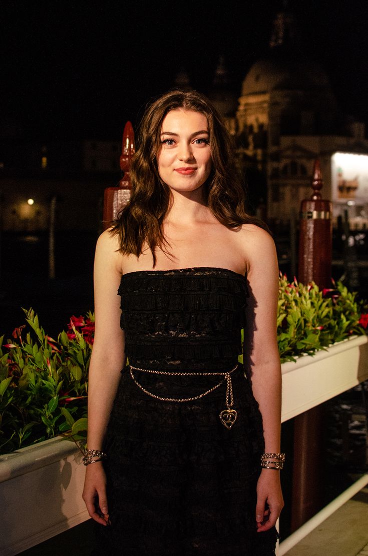 a woman in a black dress posing for the camera at night with her hands on her hips