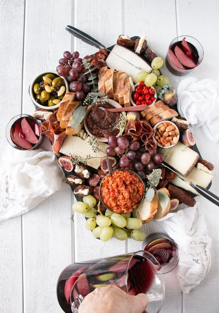 a platter filled with cheeses, meats and fruit next to wine glasses