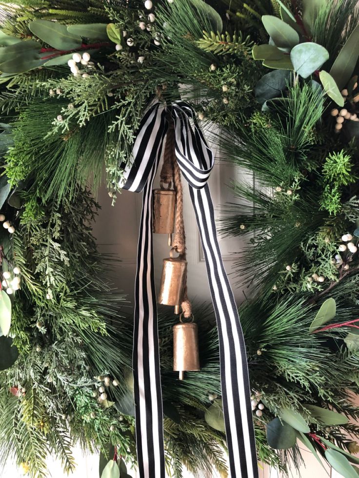 a christmas wreath with bells and greenery on the front door, tied with a black and white ribbon