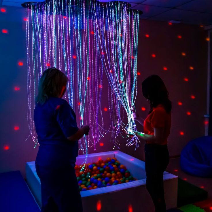 two women standing next to each other in front of a ball pit filled with balls