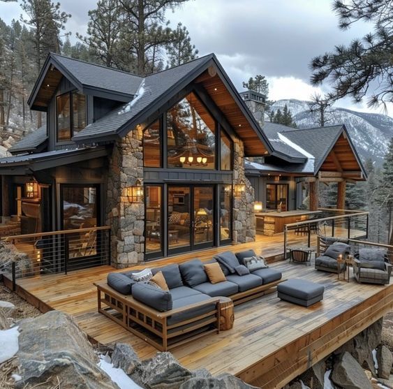 a large wooden deck with couches and tables on it in front of a mountain home