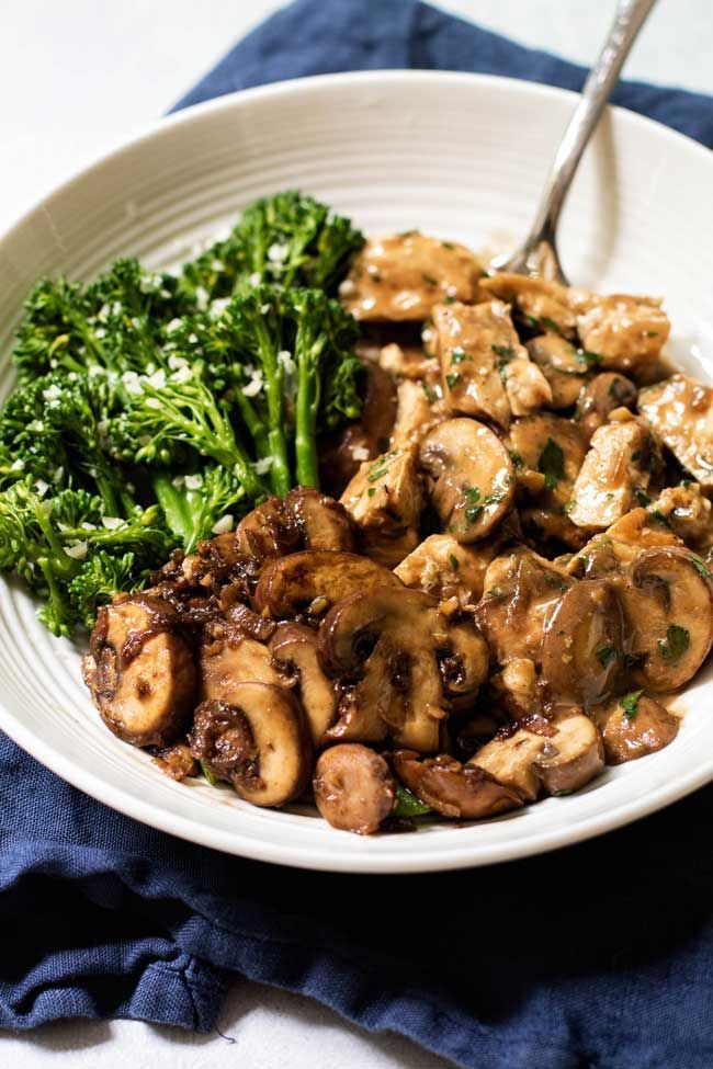 a white bowl filled with mushrooms and broccoli on top of a blue towel