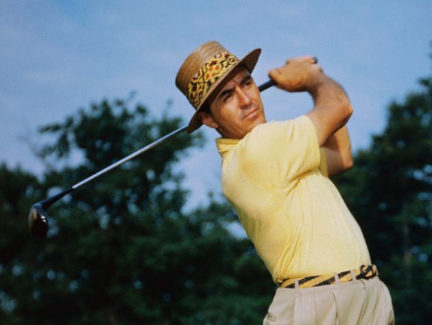 a man swinging a golf club with trees in the background