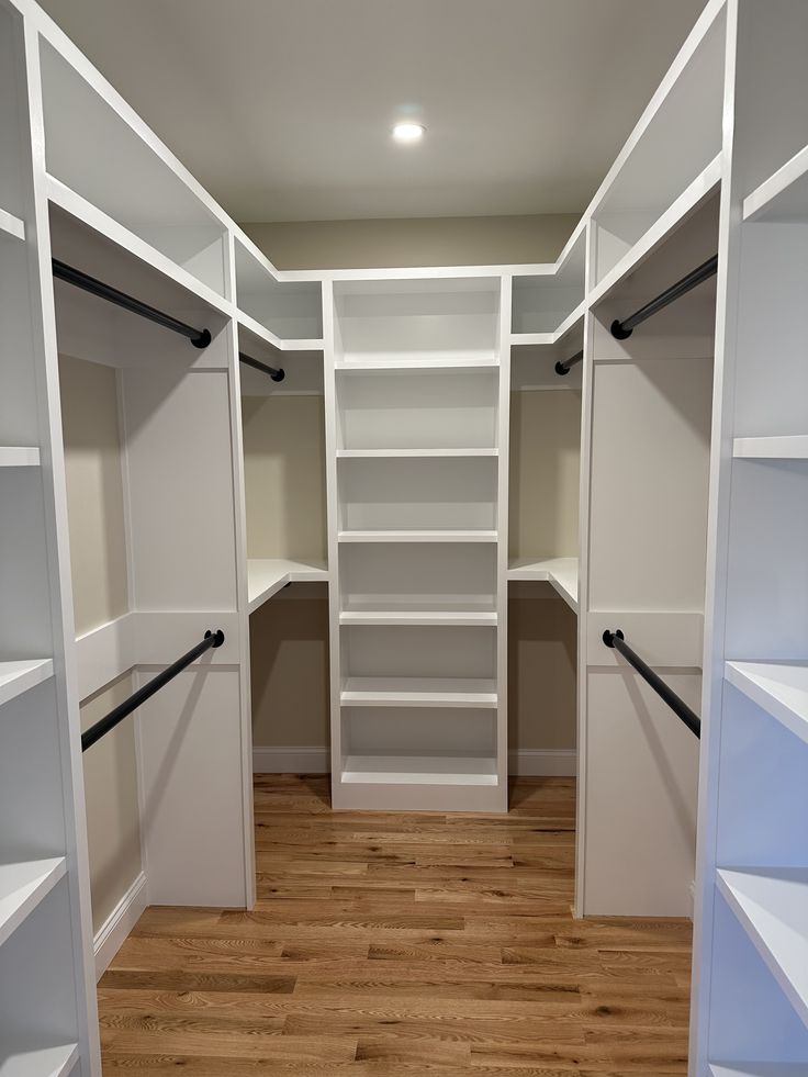 an empty walk in closet with white shelving and wood flooring on the side