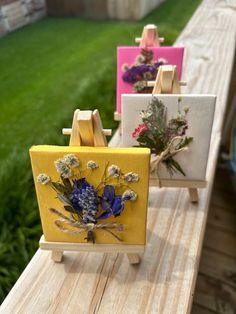 three easels with flowers painted on them sitting on a wooden table in the grass