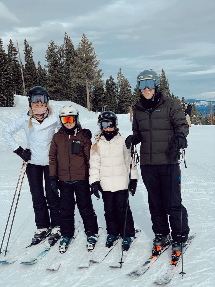 three adults and two children on skis posing for a photo in the snow with trees behind them