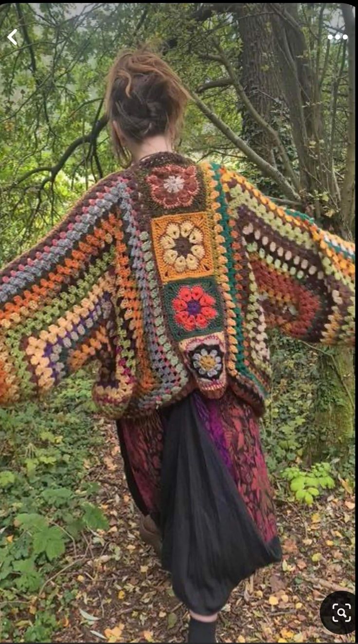 a woman is walking in the woods wearing a crocheted jacket with flowers on it