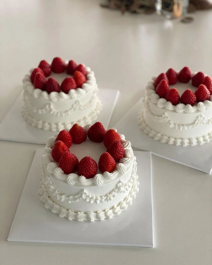 three small cakes with white frosting and raspberries on top are sitting on the table