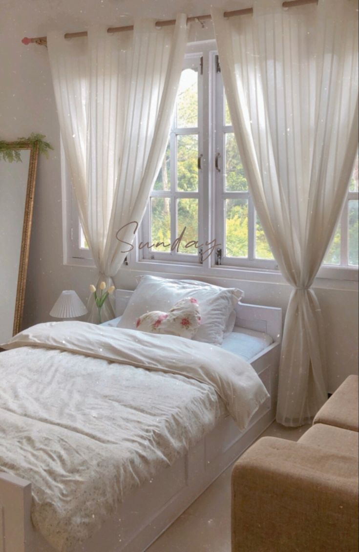 a white bed sitting next to a window in a room with curtains on the windowsill