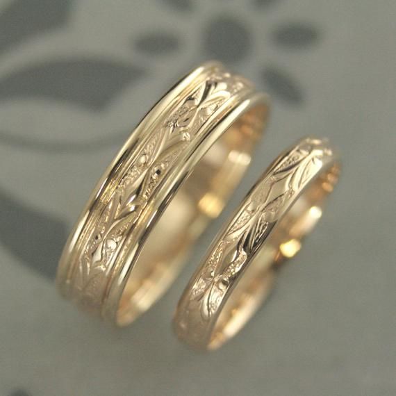 two gold wedding bands with floral designs on them, one has a diamond in the center