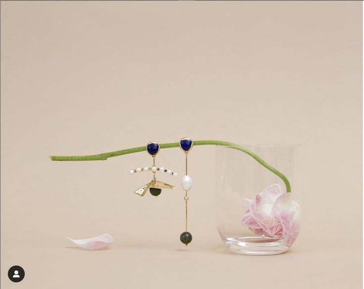 a vase with flowers and jewelry hanging from it's side on a white surface