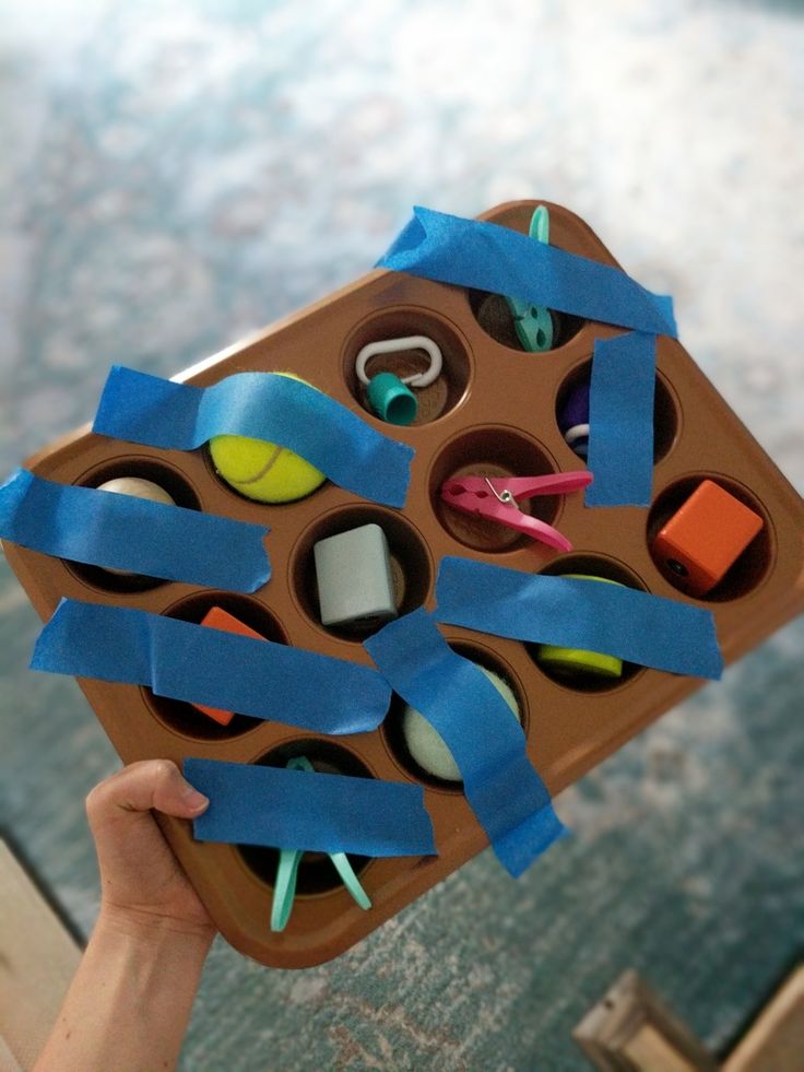 a person holding up a cardboard box with scissors and pens in it on top of a table