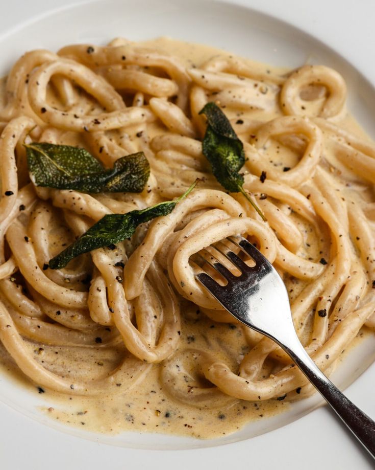 a white plate topped with pasta covered in sauce and spinach next to a fork