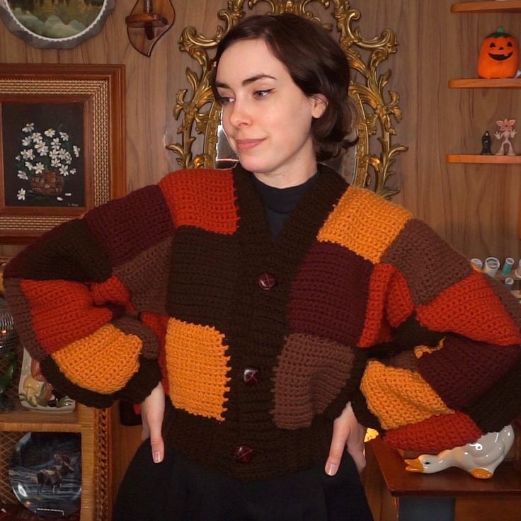 a woman standing in front of a wooden wall wearing a multicolored knitted sweater