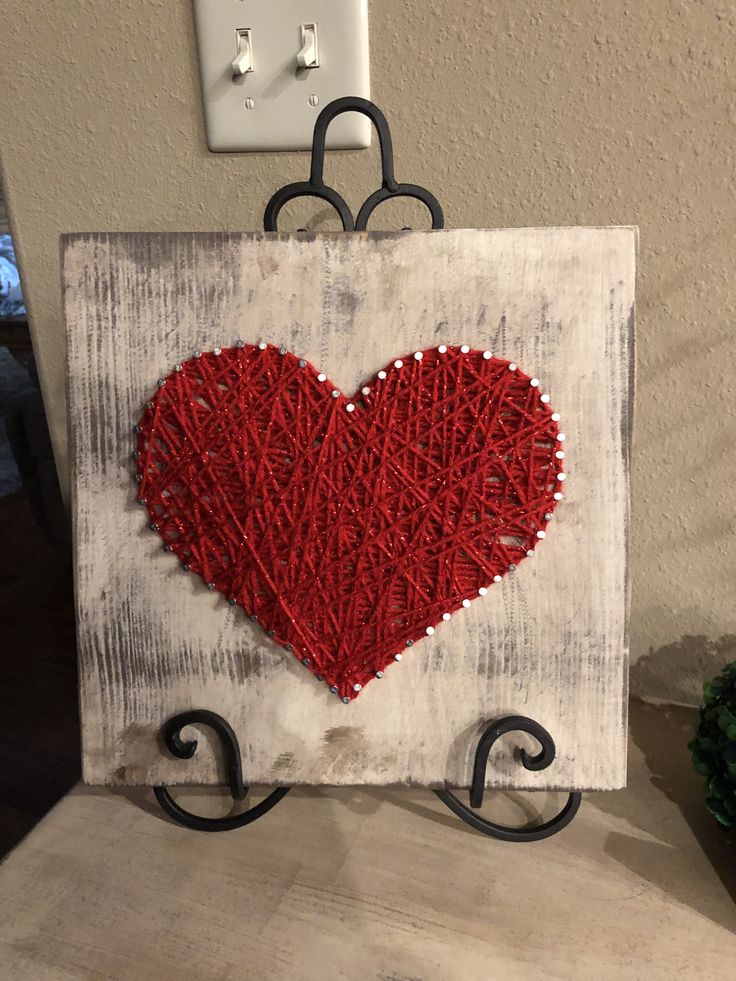 a red heart is hanging on a white wooden sign with black iron brackets and a light switch