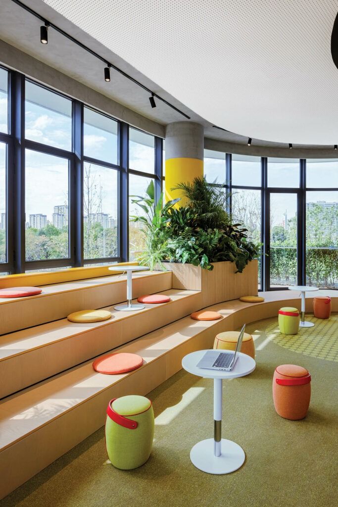 the interior of an office building with large windows and colorful seating on the floor, along with potted plants