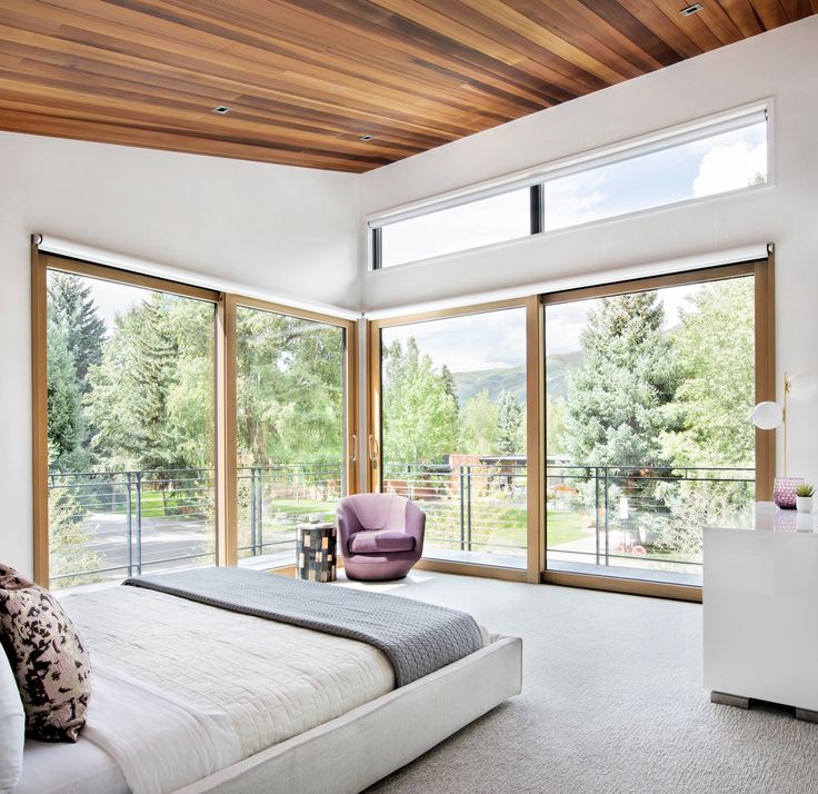 a bedroom with large windows, a bed and a chair in front of the sliding glass doors