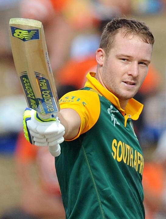 a man in green and yellow jersey holding a cricket bat on his left hand, looking at the camera