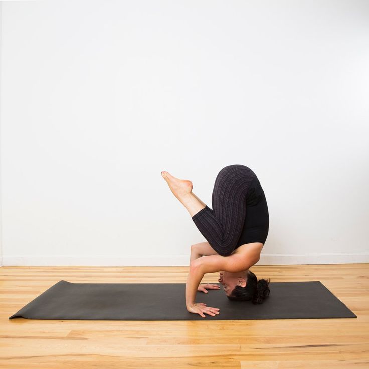 a person doing yoga on a mat in front of a white wall and hardwood floor