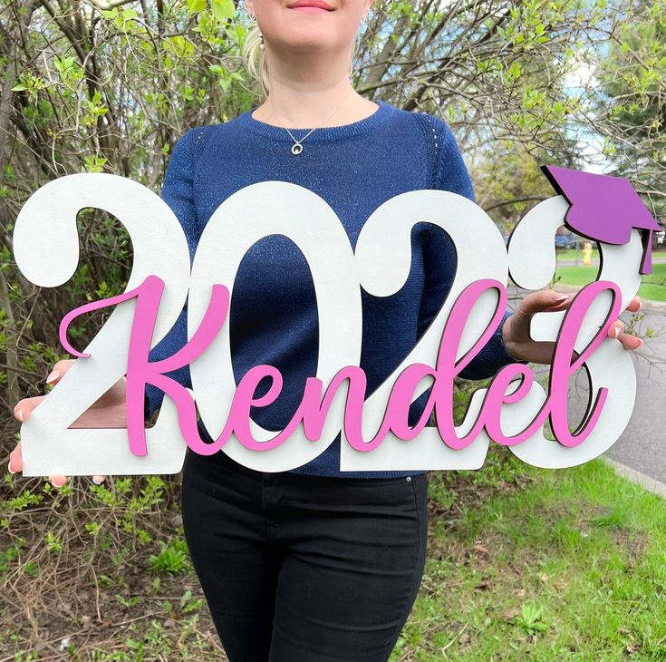 a woman holding up a sign that says kendele in pink and white letters