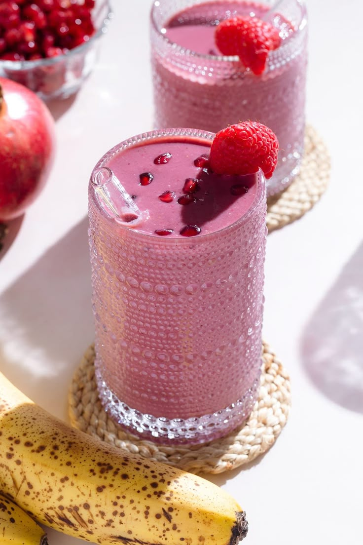 two glasses of smoothie with raspberries on the rim and one glass filled with fruit