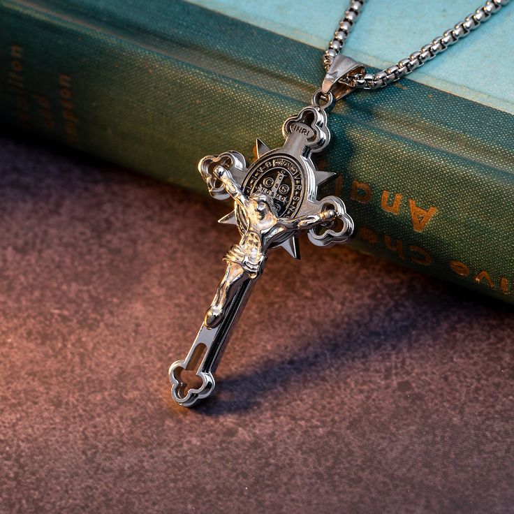 a silver cross with a clock on it is sitting next to a book and chain