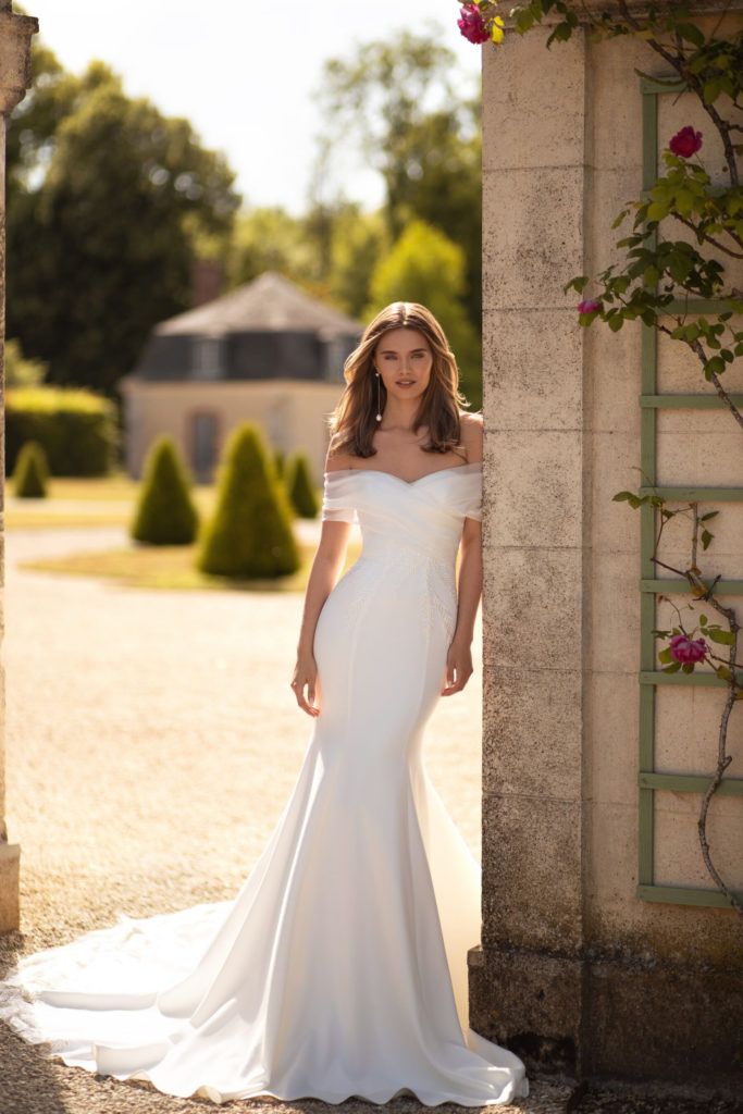 a woman in a white wedding dress leaning against a wall with her hands on her hips