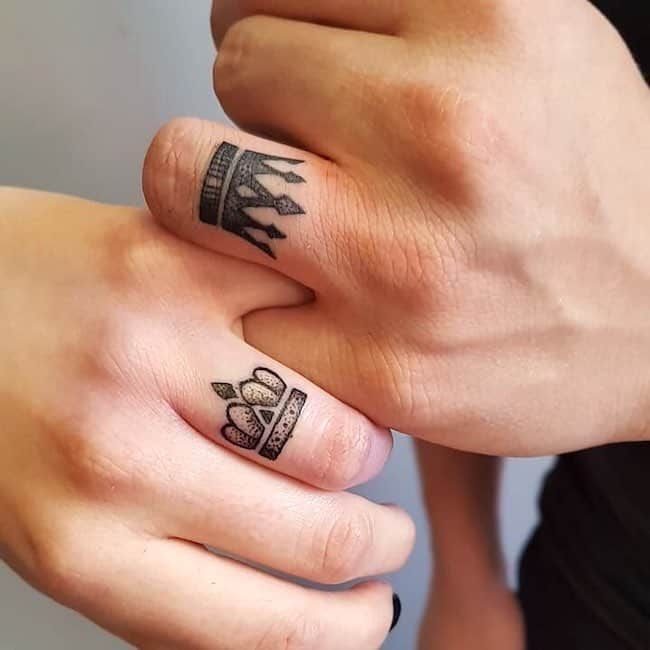 two people with tattoos on their fingers holding each other's hands and one has a crown tattoo on it