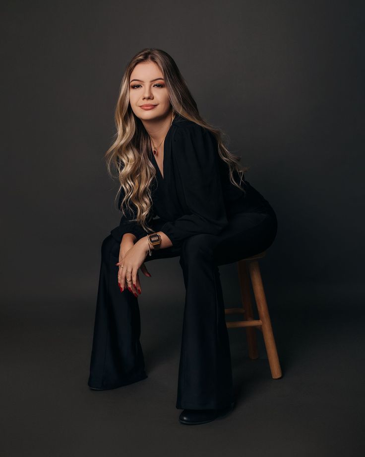 a woman sitting on top of a wooden chair wearing black pants and a black shirt