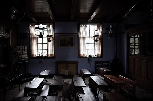 an empty table and benches in a dark room with two windows on either side of it