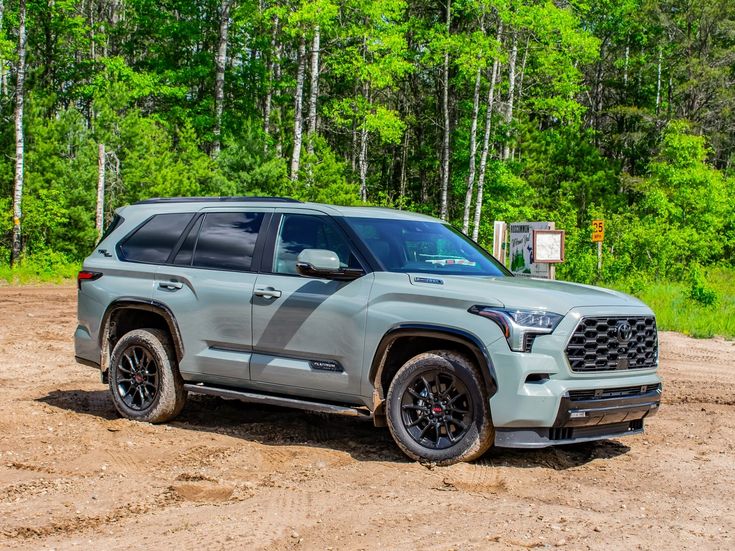 a gray toyota suv parked on top of a dirt road in front of some trees